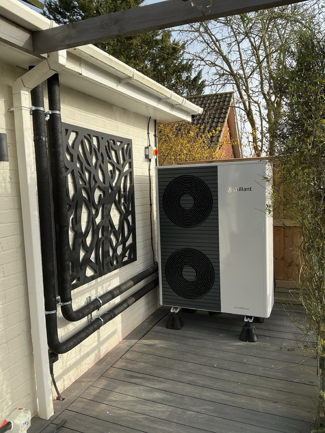 Air source heat pump on garden decking with neat insulated pipework